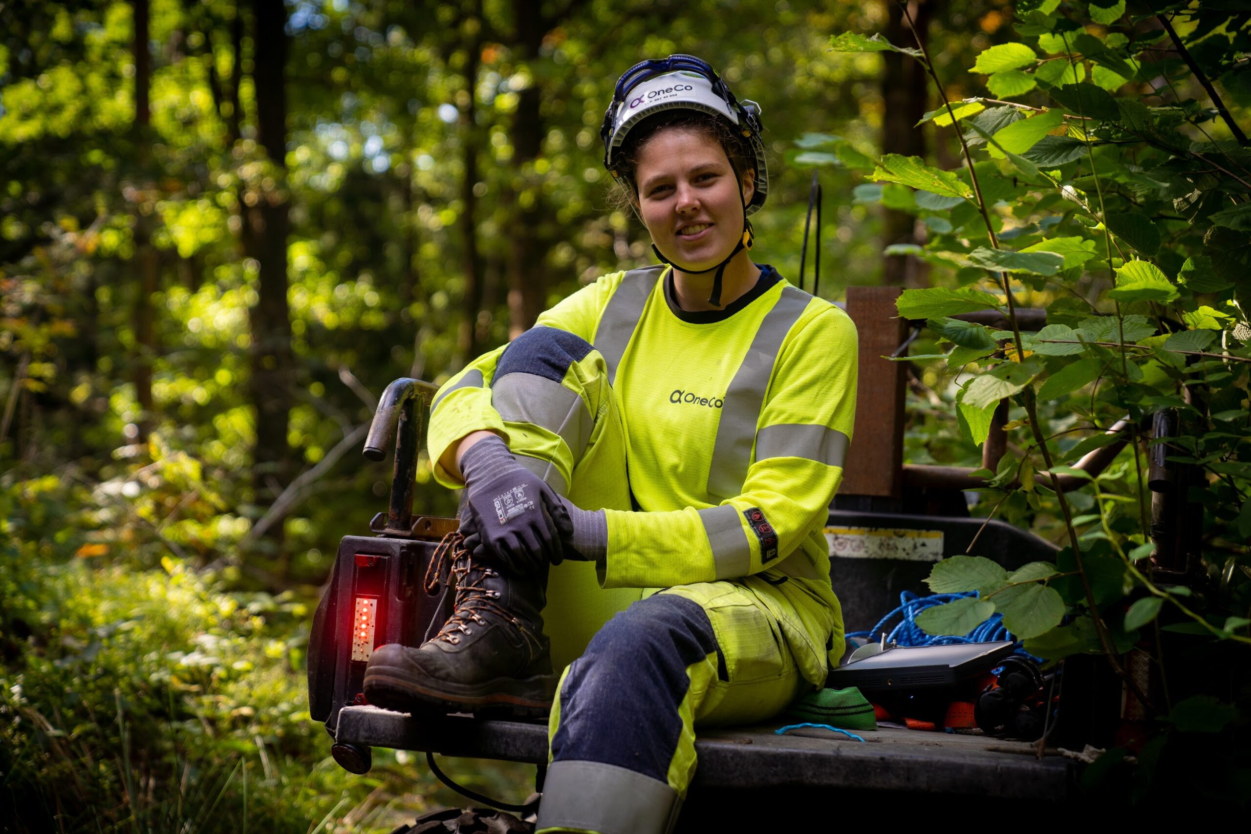 A OneCo worker is sitting in the back of a 4WD motorbike smiling at the camera.