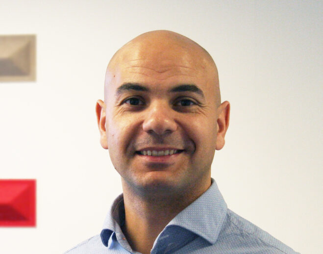 Adam Salman i ljusblå skjorta med vit och röd bakgrund.