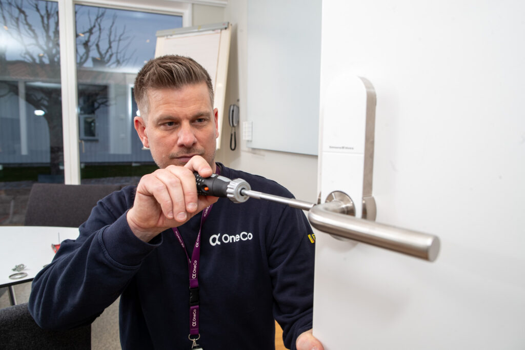 OneCo-tekniker installerar digitalt lås i en dörr med hjälp av en skruvmejsel.