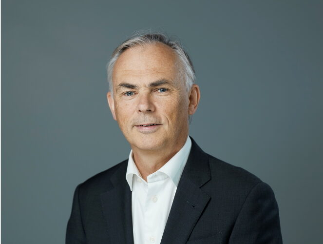 Tore Sjursen i svart kavaj och vit skjorta. Grå bakgrund.