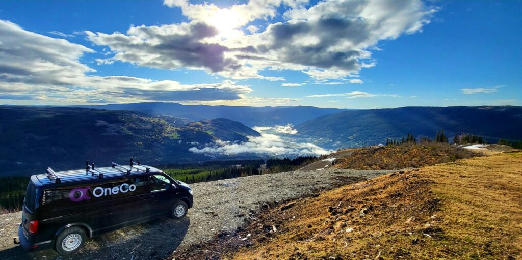 Svart OneCo-bil på en höjd med utsikt över berg och vatten.