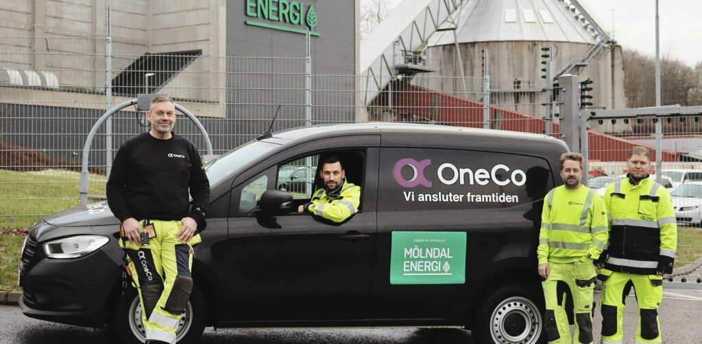 Tre OneCo-tekniker bredvid en OneCo-bil med Mölndal Energis logga på. I bilen sitter ytterligare en OneCo-tekniker. I bakgrunden syns en byggnad med Mölndal Energis logga på.