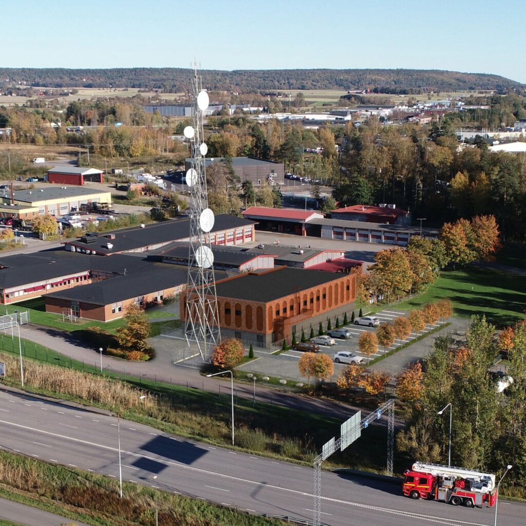 Illustration snett ovanifrån av tegelbyggnader med en telemast och kommunikationslösningar. Framför byggnaderna syns en väg med en brandbil.