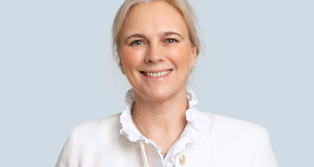 Kvinna i ljusa kläder som ler mot kameran. Ljus bakgrund.