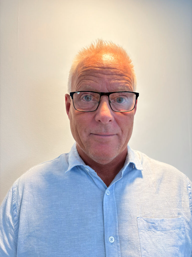 Man med glasögon och blå skjorta som tittar in i kameran.